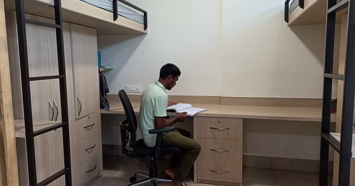 A resident studying in a furnished hostel room